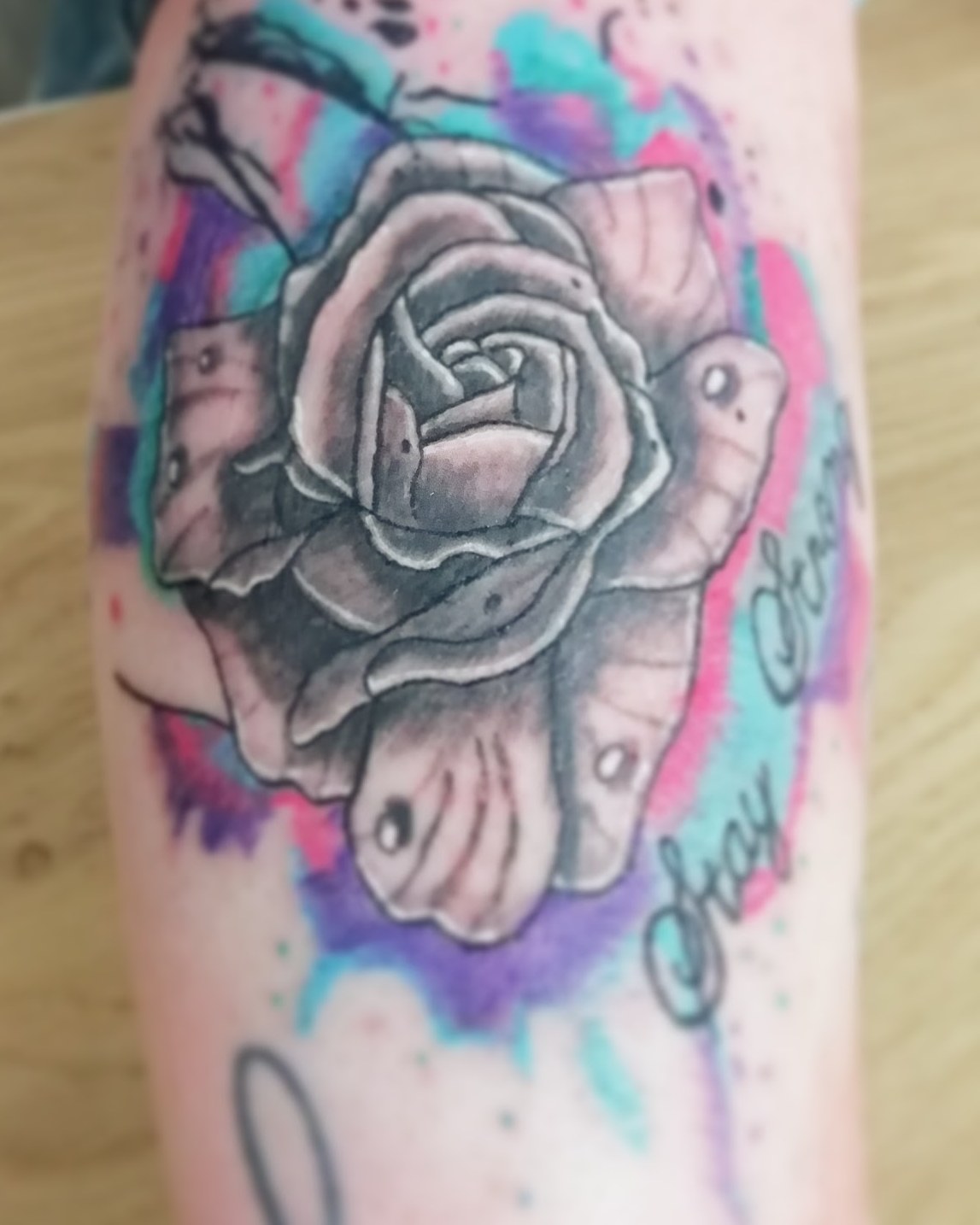 Zwart-grijze roos met een aquarelrand in roze, paars en turquoise op de onderarm